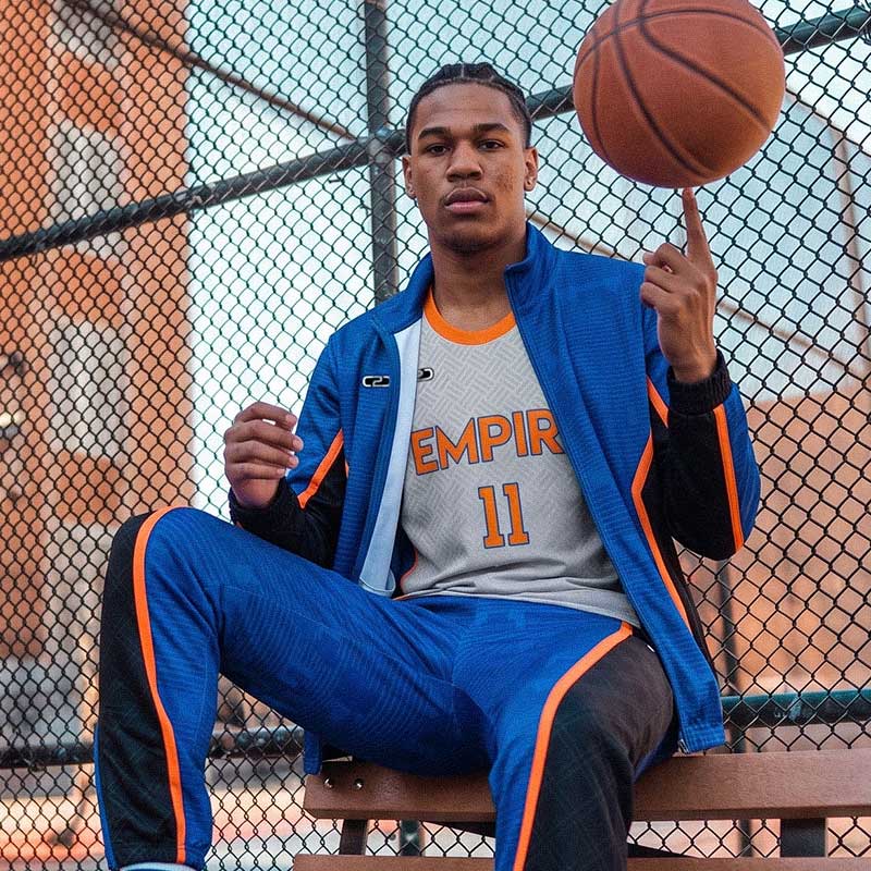 Person holding a basketball on a court wearing an 'EMPIRE 11' C2C Sports custom sublimated basketball singlet and trackpants.